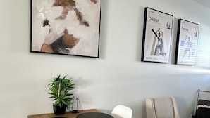 A dining area with a wooden table, black circular placemats, white chairs, and two framed posters on the wall. - Beautiful Modern Two Bedroom Apartment  (Brandon)