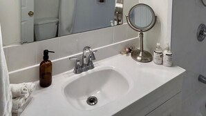 A bathroom with a white sink, a large mirror, and a handheld mirror. There are multiple light fixtures above the mirror. - Beautiful Modern Two Bedroom Apartment  (Brandon)