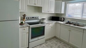 A kitchen with white cabinets, a stove, a microwave, and a sink. - Beautiful Modern Two Bedroom Apartment  (Brandon)