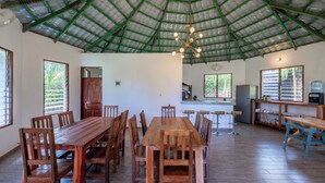 A spacious room with a high green metal roof, a wooden dining table with chairs, a kitchen area with a refrigerator, and a water dispenser. - Babylon Gardens (Diani Beach)