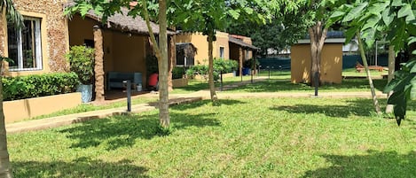 A courtyard with a thatched-roof building, a palm tree, and a well-maintained lawn.