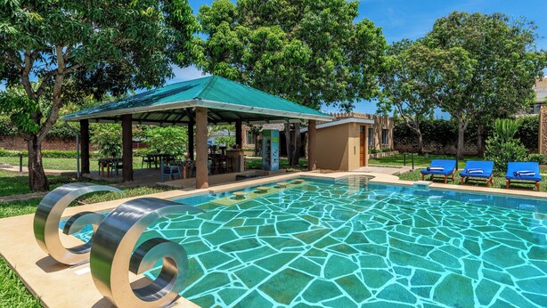 A swimming pool with a green roofed pavilion, lounge chairs, and a grassy area. - Babylon Gardens (Diani Beach)