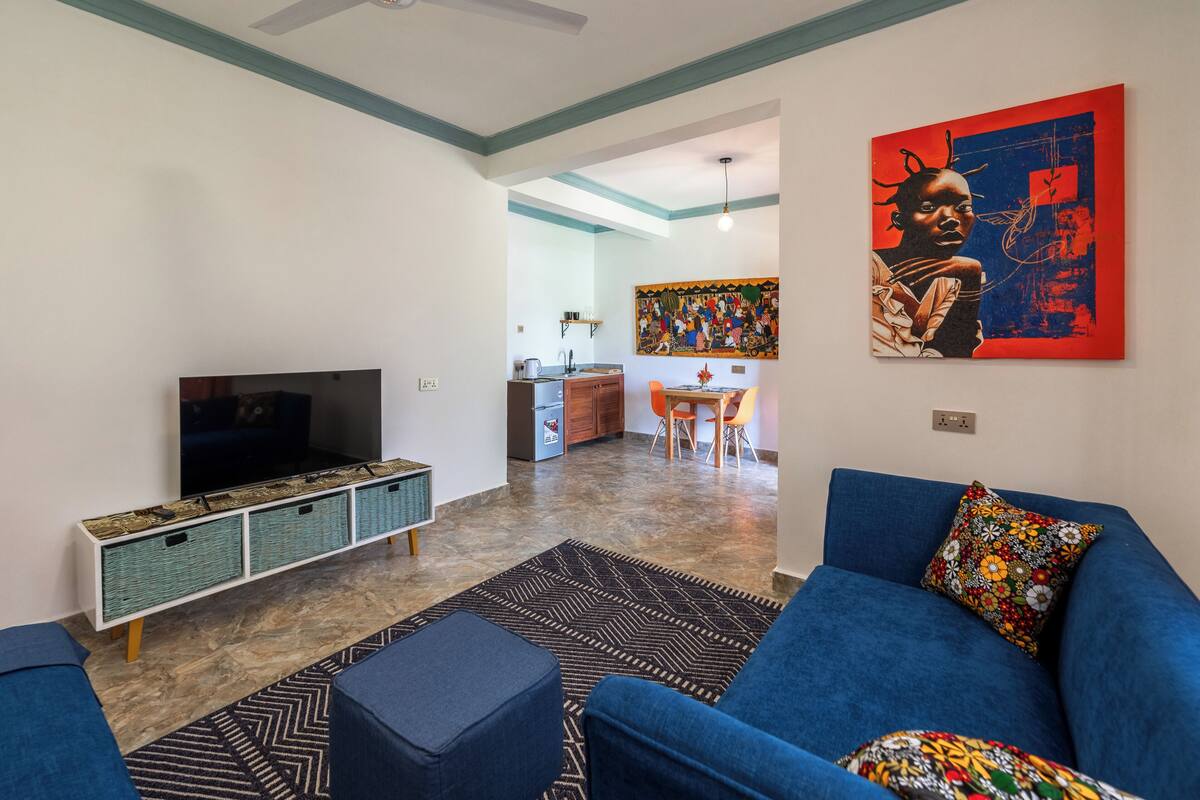 A modern living room with a blue sofa, a television, and a kitchen in the background.