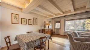 A dining area with a wooden table and chairs, framed botanical prints on the wall, a window with a view of trees, and a radiator below. - Casa Funivia, Casa Funivia, close to the center and the cableway (Cortina d´Ampezzo)