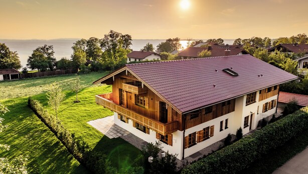 A two-story house with a red-tiled roof, wooden exterior, and a balcony.