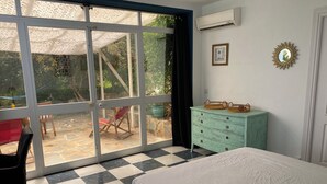A bedroom with a checkered floor, a bed, a sliding glass door leading to an outdoor area with chairs and a table, a green dresser, and an air conditioning unit on the wall. - Accommodation with private terrace in tropical garden,  (Estepona)