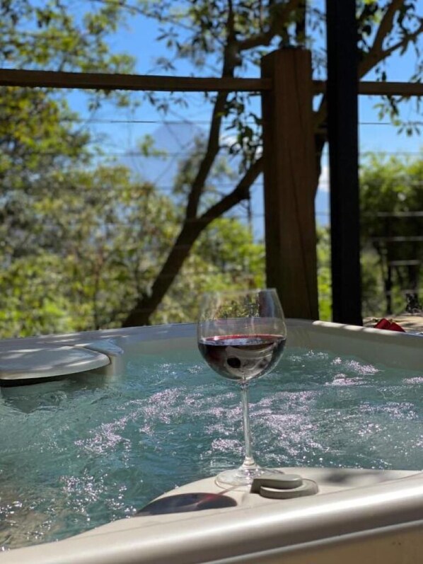 A glass of red wine on a hot tub with a clear view of trees and a wooden structure in the background.
