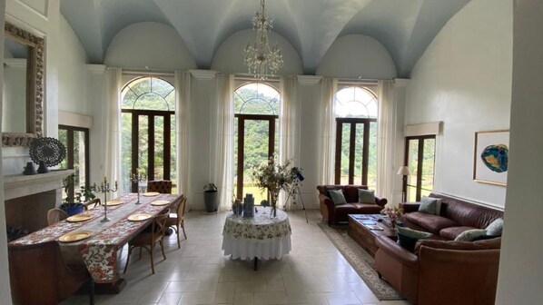 A spacious room with a dining table set for six, a sofa, and a chandelier.