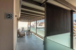 A balcony with a glass partition, a sofa, a small table, and a chair. - Harma City Living (Chania)