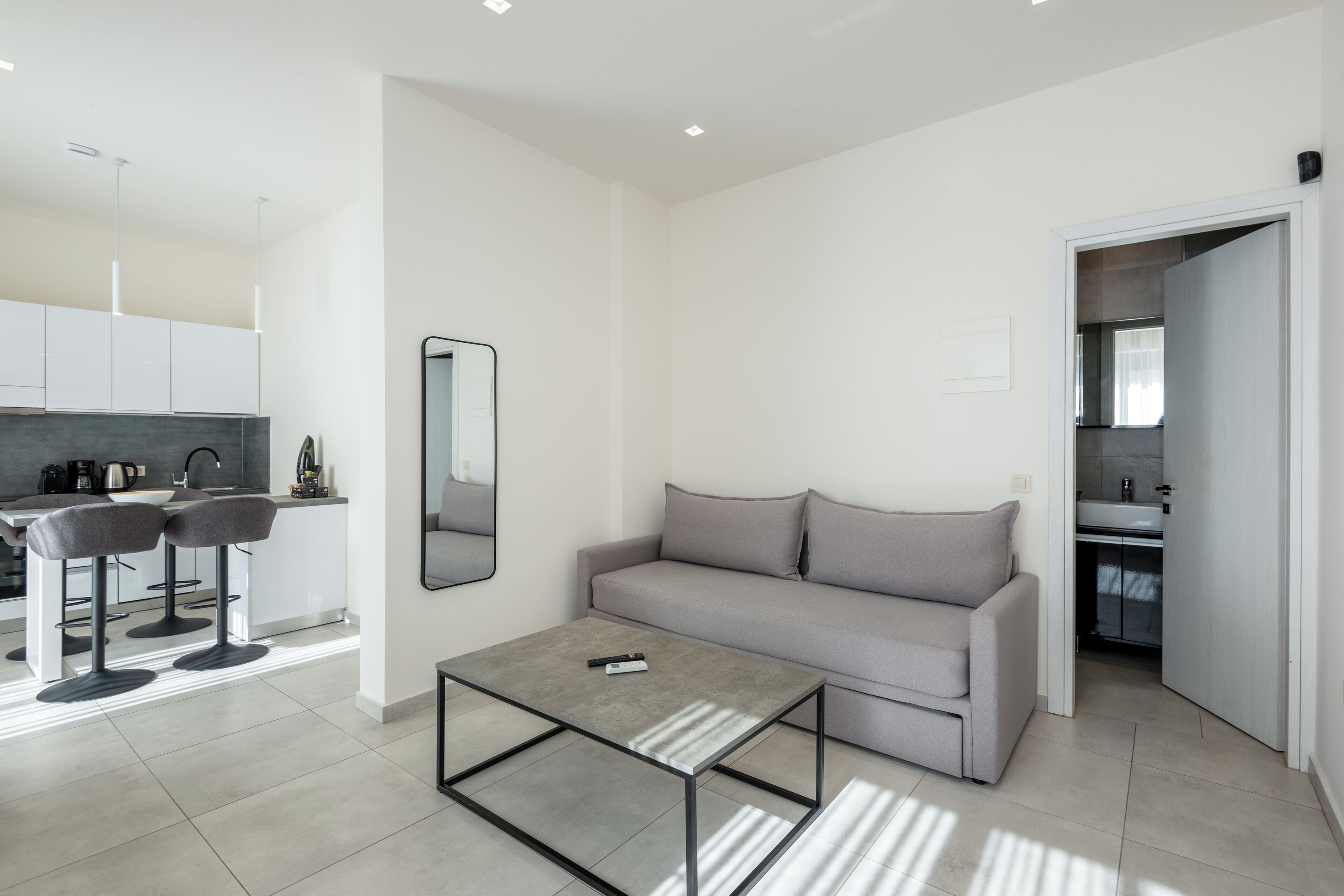 Un salon moderne avec un canapé gris, une table basse et un coin cuisine à l’arrière-plan.