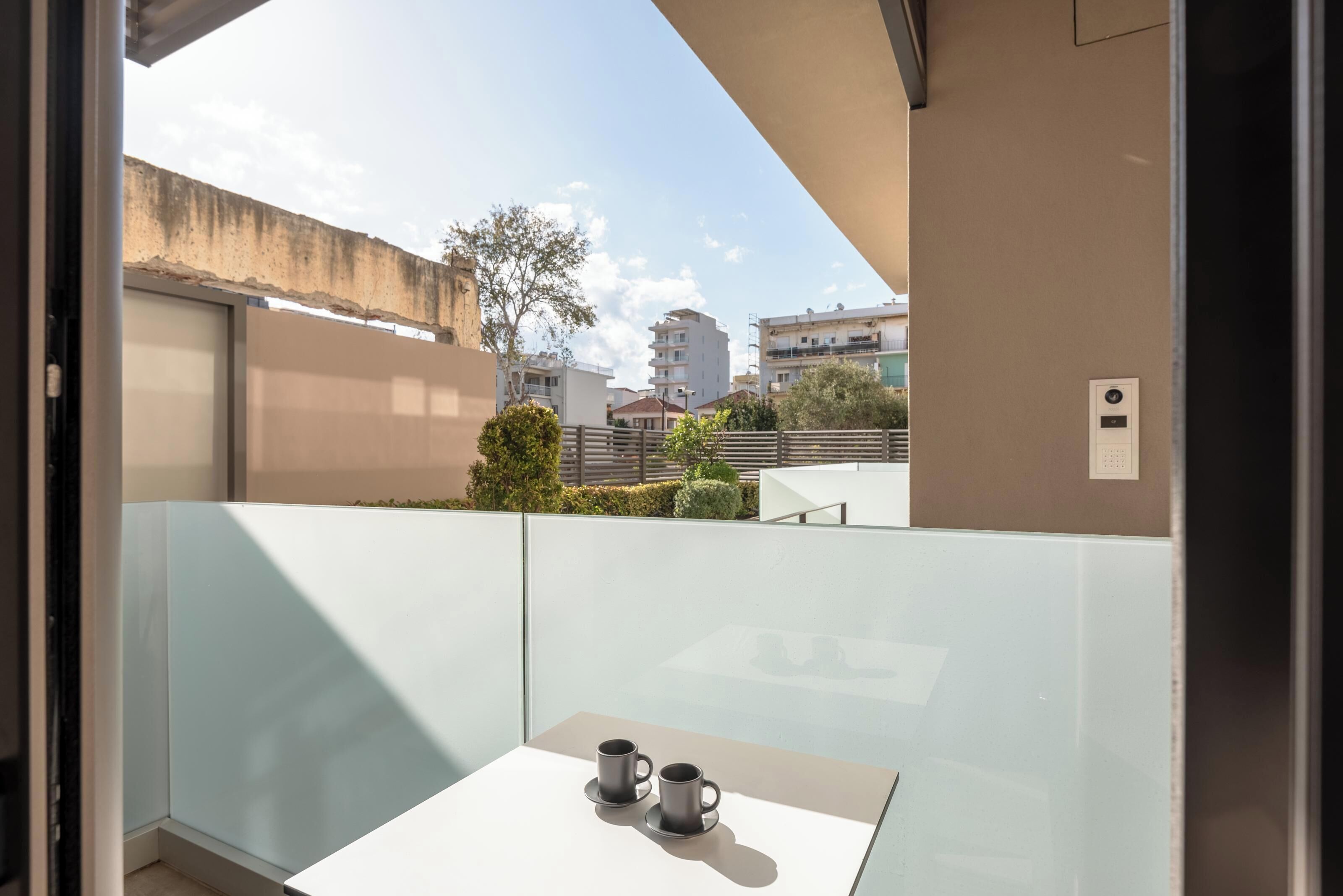 Ein Balkon mit Tisch und zwei Tassen, mit Blick auf ein Wohngebiet mit Gebäuden und Grünflächen.
