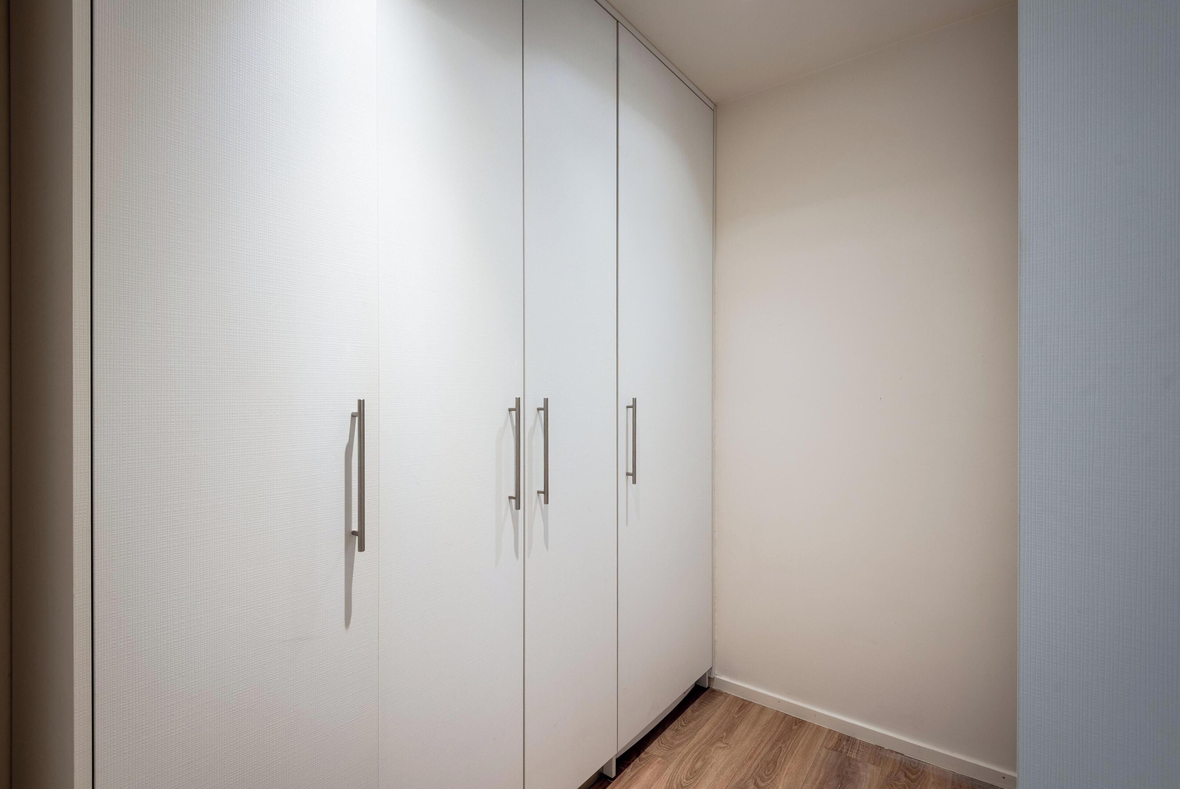 Habitación de esquina con armario, piso de madera y pared lisa.