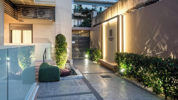 A modern building with a glass facade, a courtyard with plants, and a well-lit entrance. - Harma City Living (Chania)