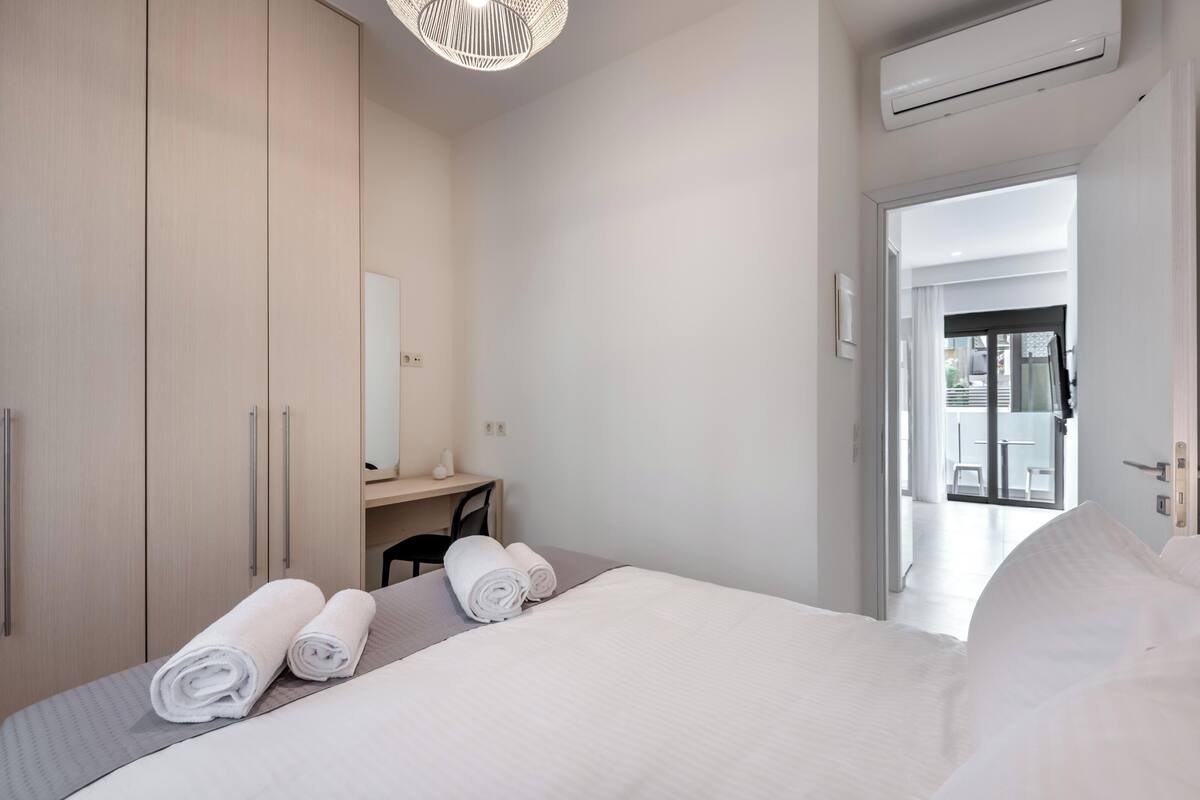 Quarto de hotel moderno com cama bem arrumada, escrivaninha com cadeira e guarda-roupa espaçoso.