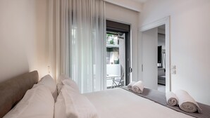 A hotel room with a large bed, a sitting area with a table and chairs, and a view of the outside balcony. - Harma City Living (Chania)