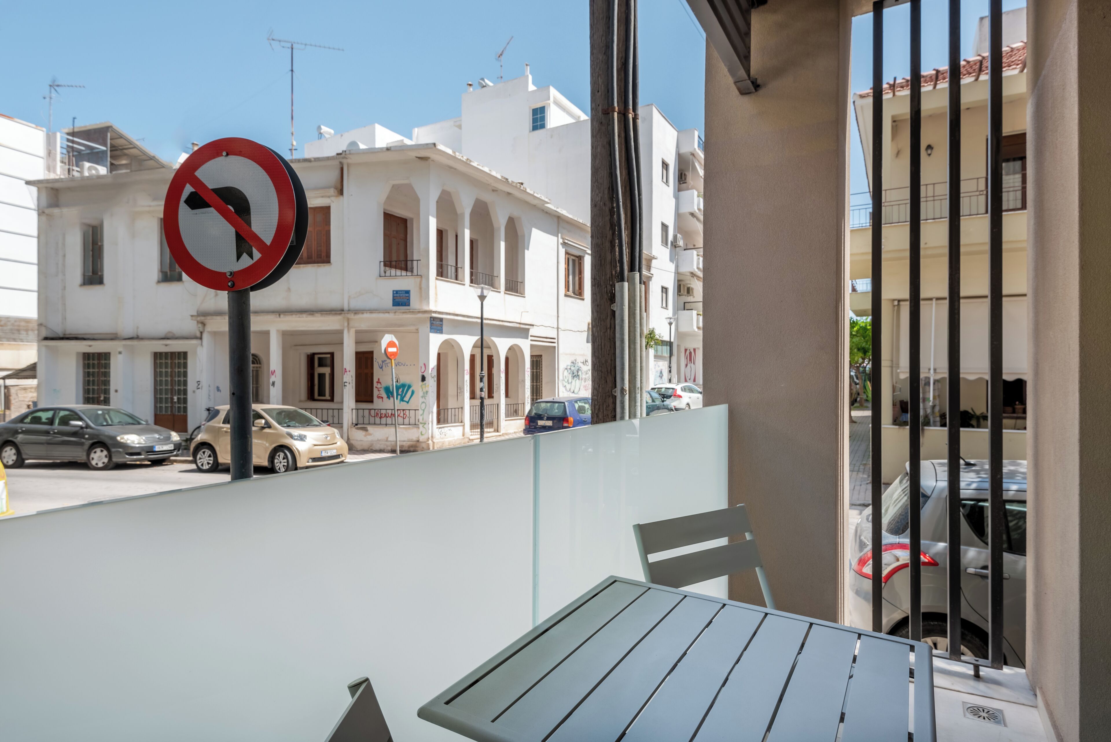 Vista desde un balcón con vista a una calle con coches estacionados y un edificio de paredes blancas y arcos.