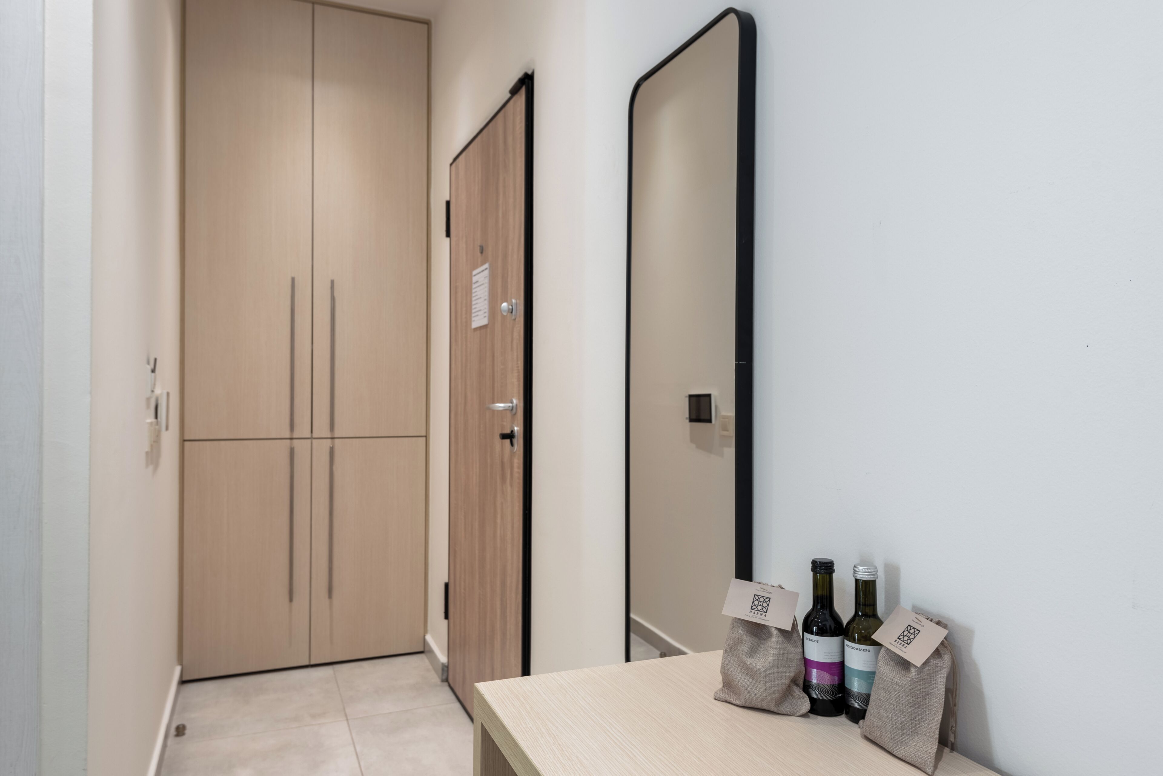 A hotel room with a wooden wardrobe, a mirror, and a table with wine bottles.
