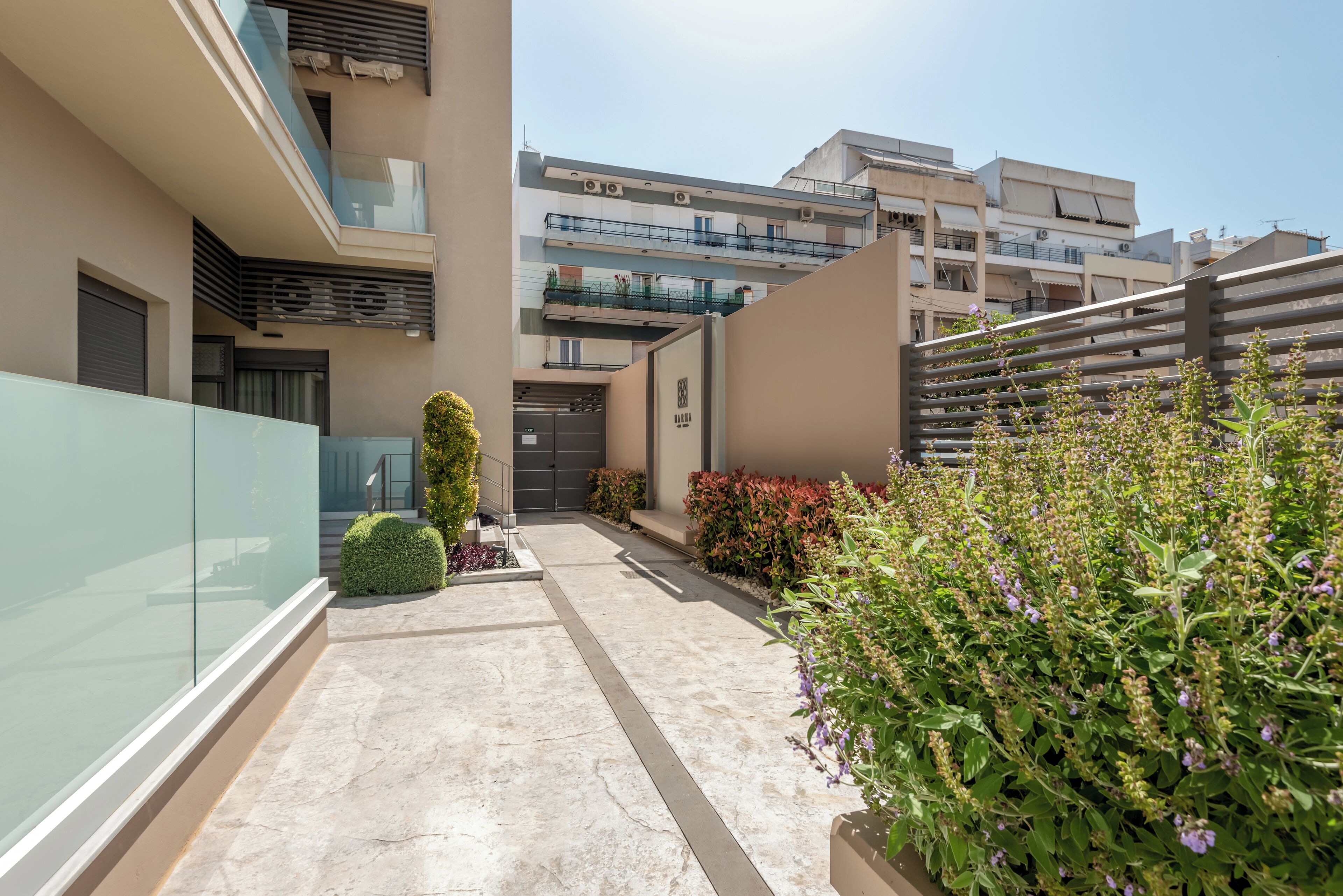 A modern residential building with a narrow pathway, glass walls, and a variety of plants.