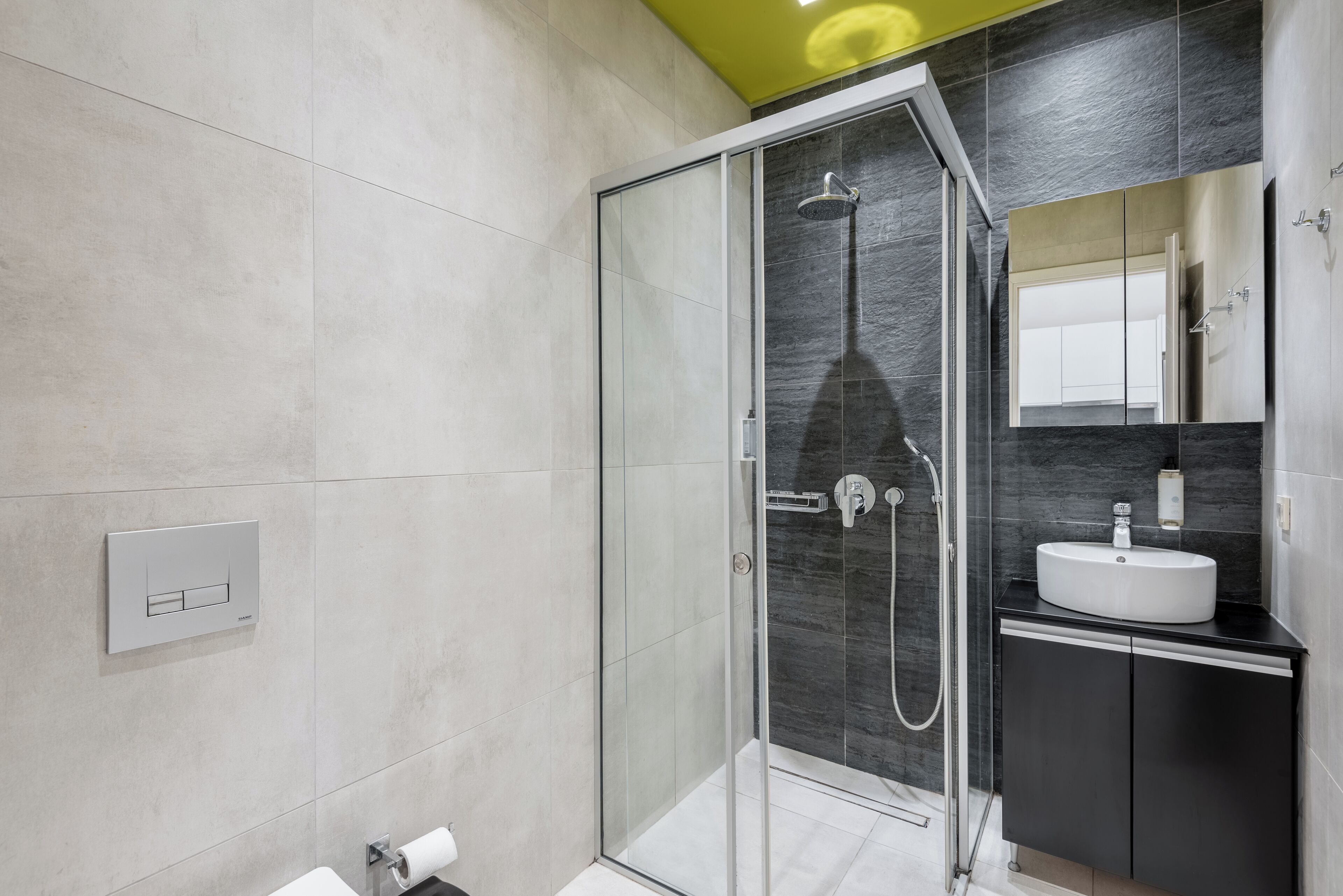A modern bathroom with a glass-enclosed shower, a white sink, and a dark-toned vanity.
