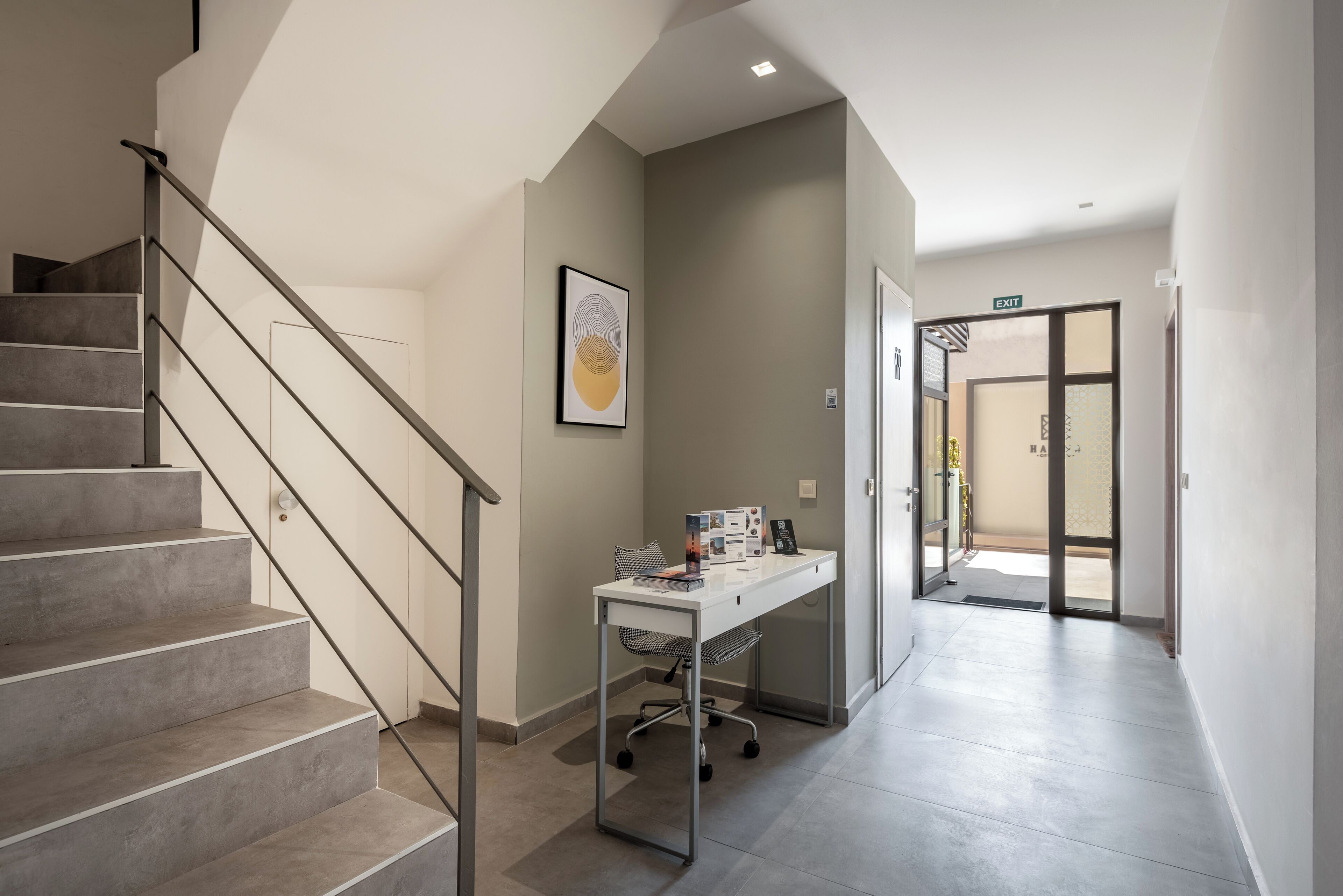 A modern interior with a staircase, a desk with a chair, and an exit door.