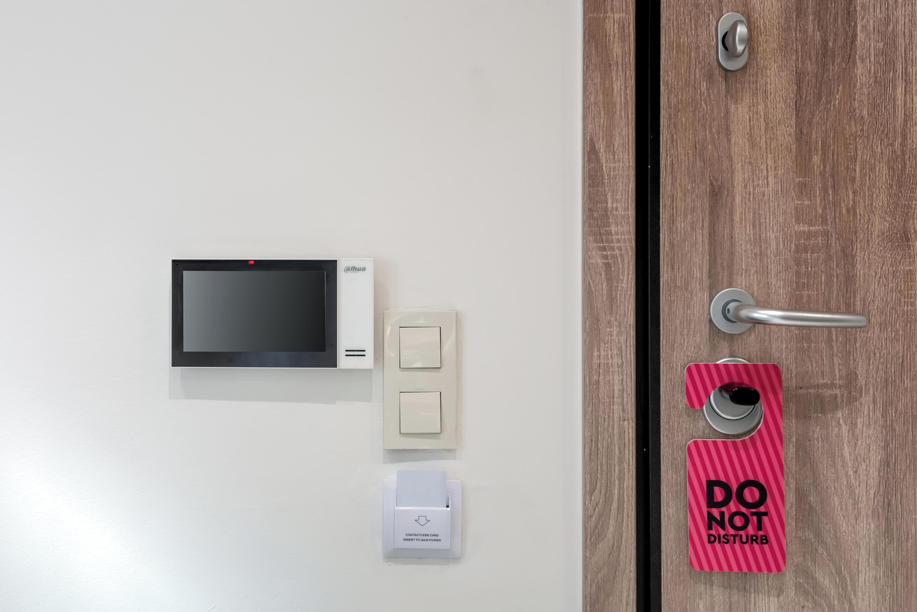 Una puerta con cerradura digital, un cartel de 'no molestar' y un lector de tarjetas.