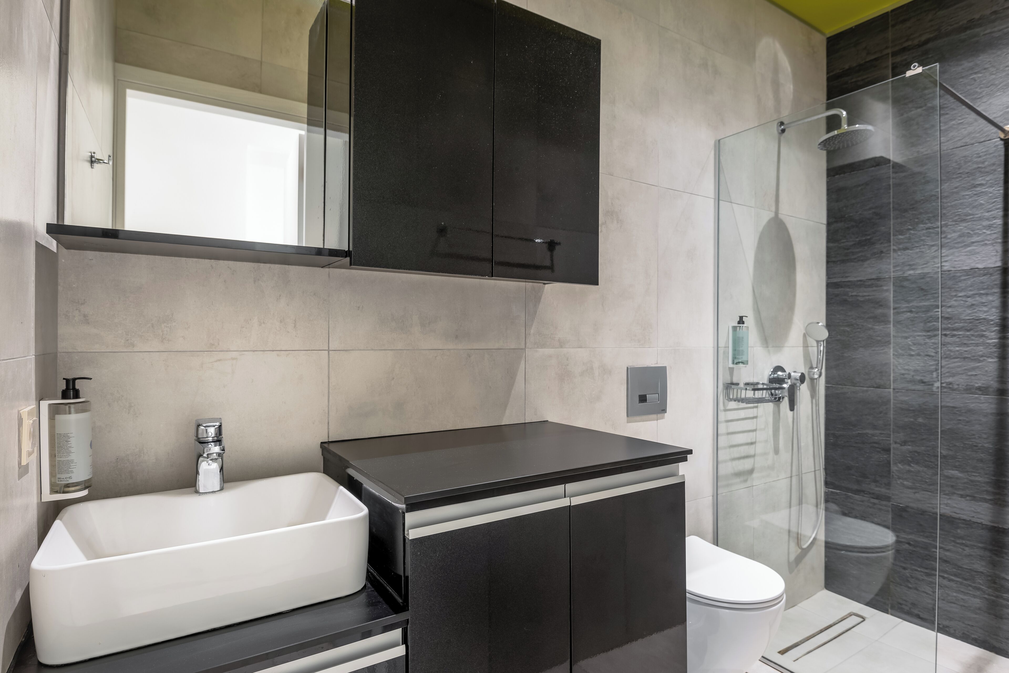 A modern bathroom with a large mirror, a black cabinet, a white sink, and a glass-enclosed shower.