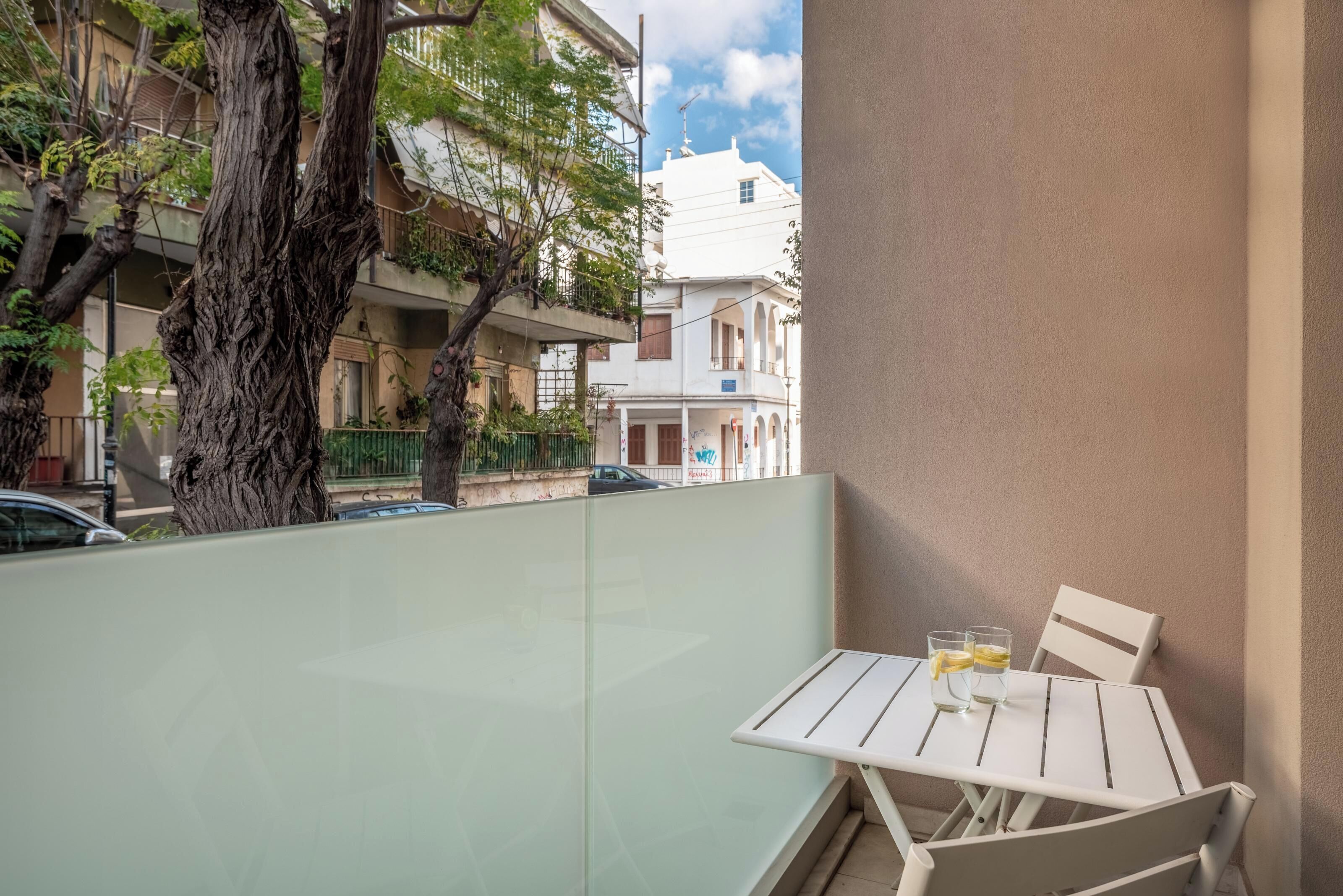 A balcony with a table and chairs, a tree, and a view of buildings in the background.