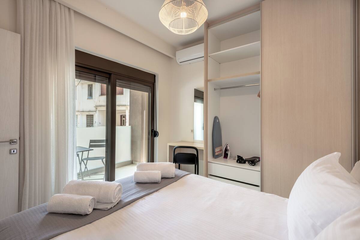 Quarto de hotel com cama, escrivaninha, cadeira, espelho e vista para a varanda externa.