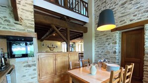 A rustic kitchen with stone walls, wooden beams, and a dining area with a table and chairs. - Spacious houses in Normandy, aux Alpes Mancelles (Moulins-le-Carbonnel)