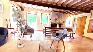 A spacious living area with a wooden coffee table, a blue sofa, and a patterned armchair. A fireplace with a clock on the wall is visible in the background. - Spacious houses in Normandy, aux Alpes Mancelles (Moulins-le-Carbonnel)