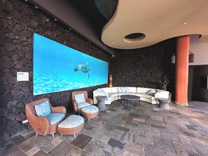 A lobby with a stone wall, a large flat-screen TV displaying a sea turtle, wicker furniture, and a curved white sofa.