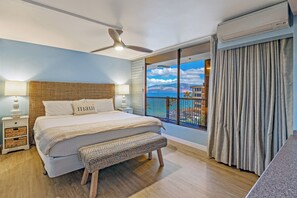 A bedroom with a bed, nightstands, a bench, a ceiling fan, and a large window with curtains.