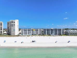 Un hotel frente al mar con varios pisos, piscina y sombrillas de playa.