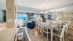 A spacious living area with a dining table, chairs, and a blue sofa. There is a kitchen area with cabinets and a countertop.