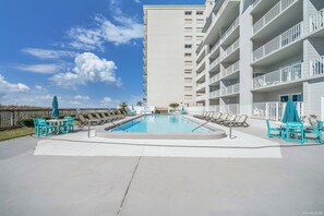 Una piscina con sillas de descanso y sombrillas, rodeada por un edificio de gran altura.