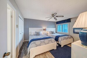 A bedroom with two beds, a ceiling fan, a window with blinds, and a bedside lamp.