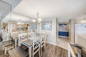 Una cocina moderna con armarios blancos, un comedor con mesa de vidrio y sillas blancas, y una lámpara de araña.
