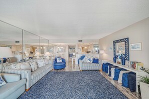 Una sala de estar moderna con un espejo grande, sofás a rayas, un sillón azul y una estantería con libros y adornos.