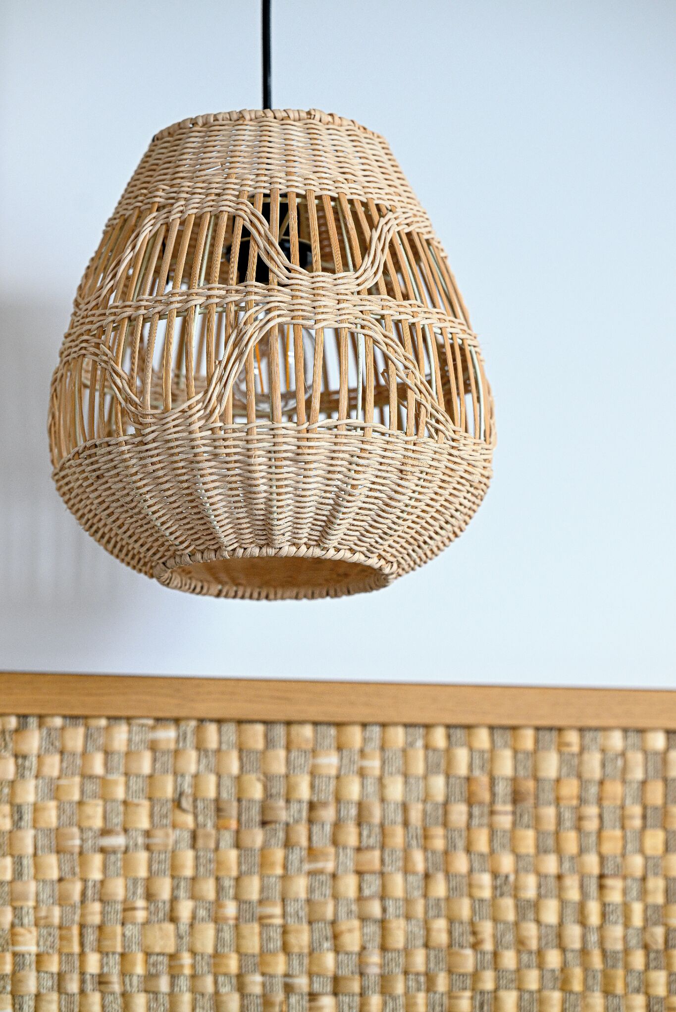 En pendel i flettet rattan med en cylindrisk form og et struktureret mønster.