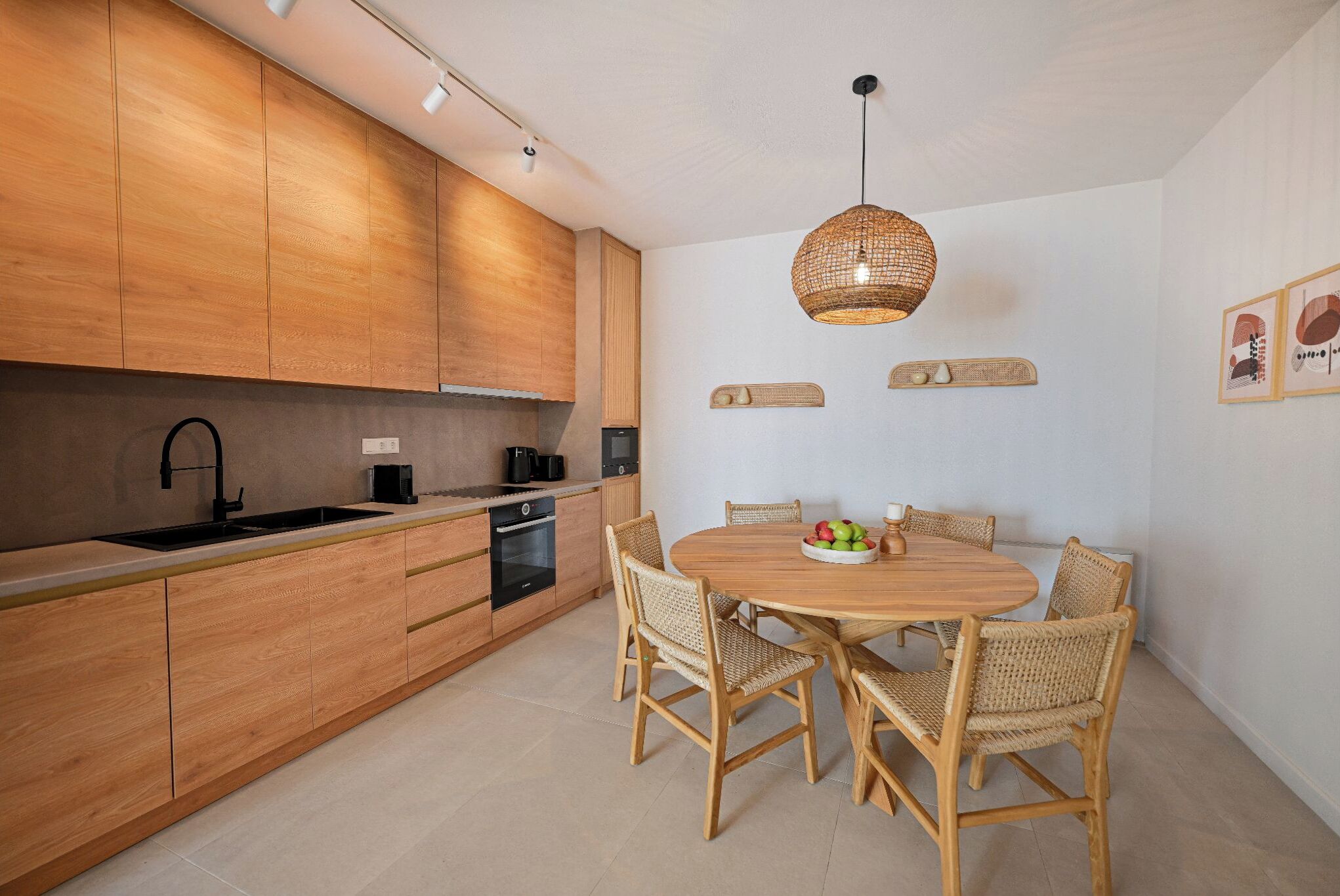 Una cocina moderna con armarios de madera, una mesa de comedor redonda, sillas de mimbre y una lámpara colgante.
