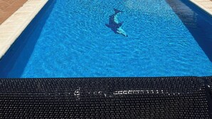 A swimming pool with clear blue water, surrounded by lounge chairs and a white building with a tiled roof. - Villa Padel (Alhaurin de la Torre)