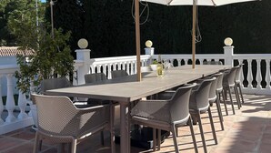 An outdoor patio with a large umbrella table and chairs, surrounded by a white balustrade and a tiled floor. - Villa Padel (Alhaurin de la Torre)