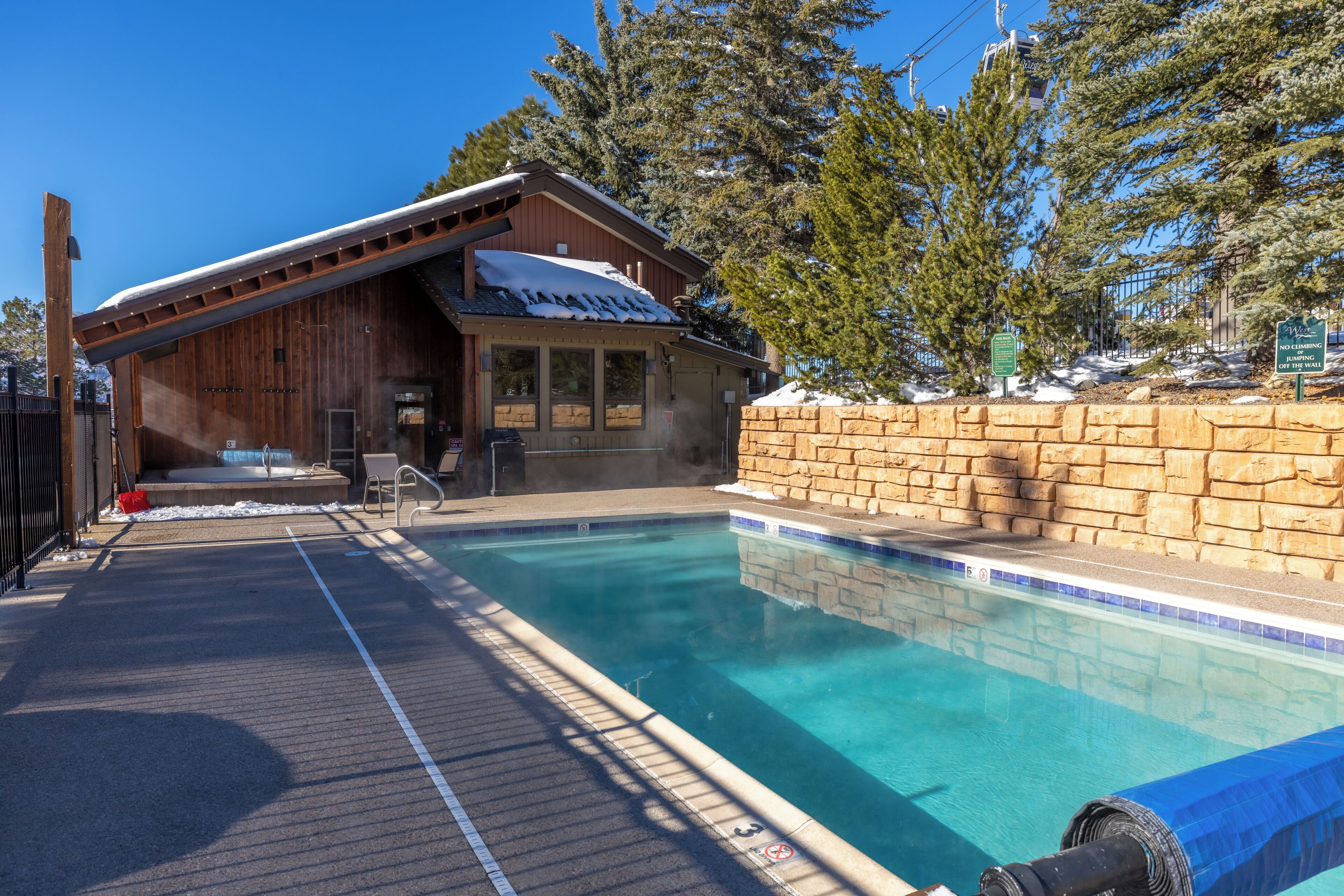 A wooden cabin with a pool, surrounded by trees and a stone wall.