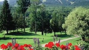 Un parcours de golf offrant une vue dégagée sur le green, les arbres et les montagnes au loin.