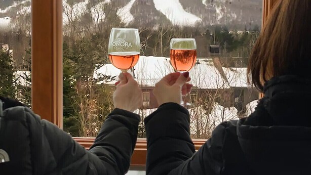Deux personnes tenant des verres de vin, avec une vue sur la montagne par la fenêtre.
