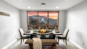 Une salle à manger dotée d’une grande fenêtre donnant sur les montagnes, d’un banc en bois et d’une table dressée pour quatre personnes.