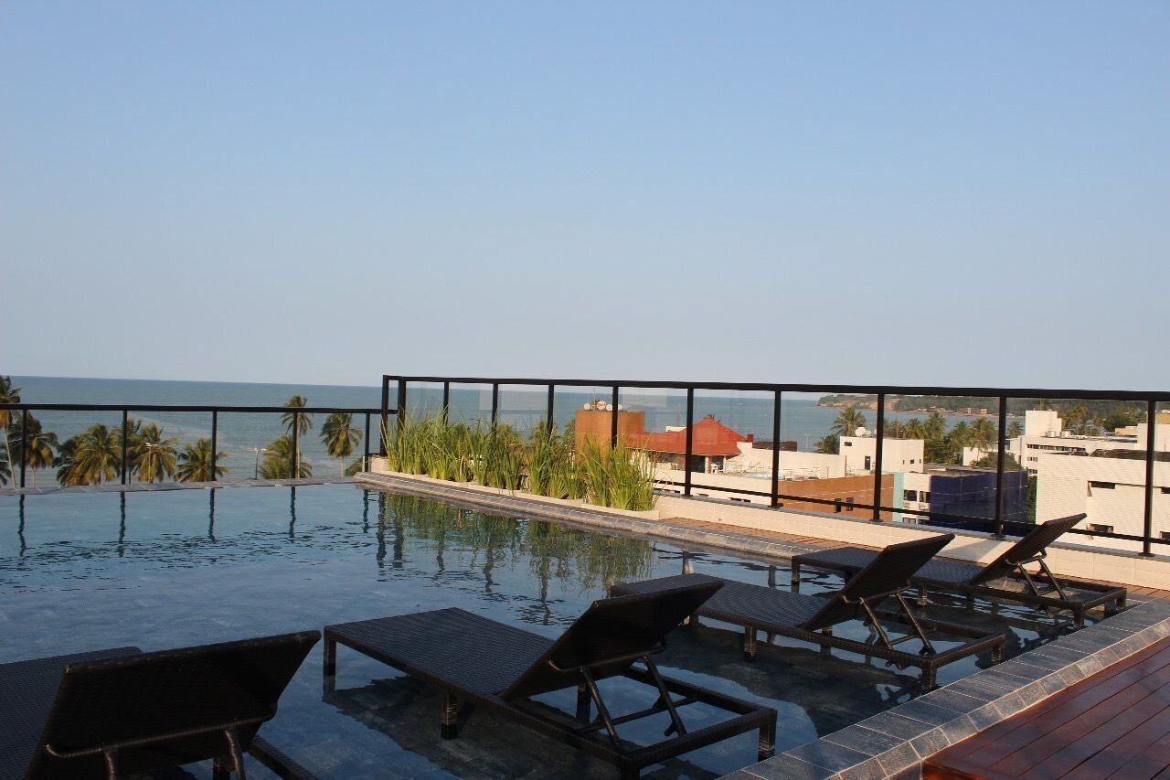 Une piscine à débordement avec des chaises longues, une vue sur la mer et des palmiers.