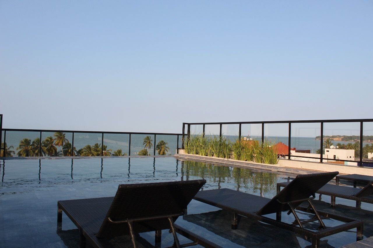An infinity pool with lounge chairs, palm trees, and a view of the ocean.