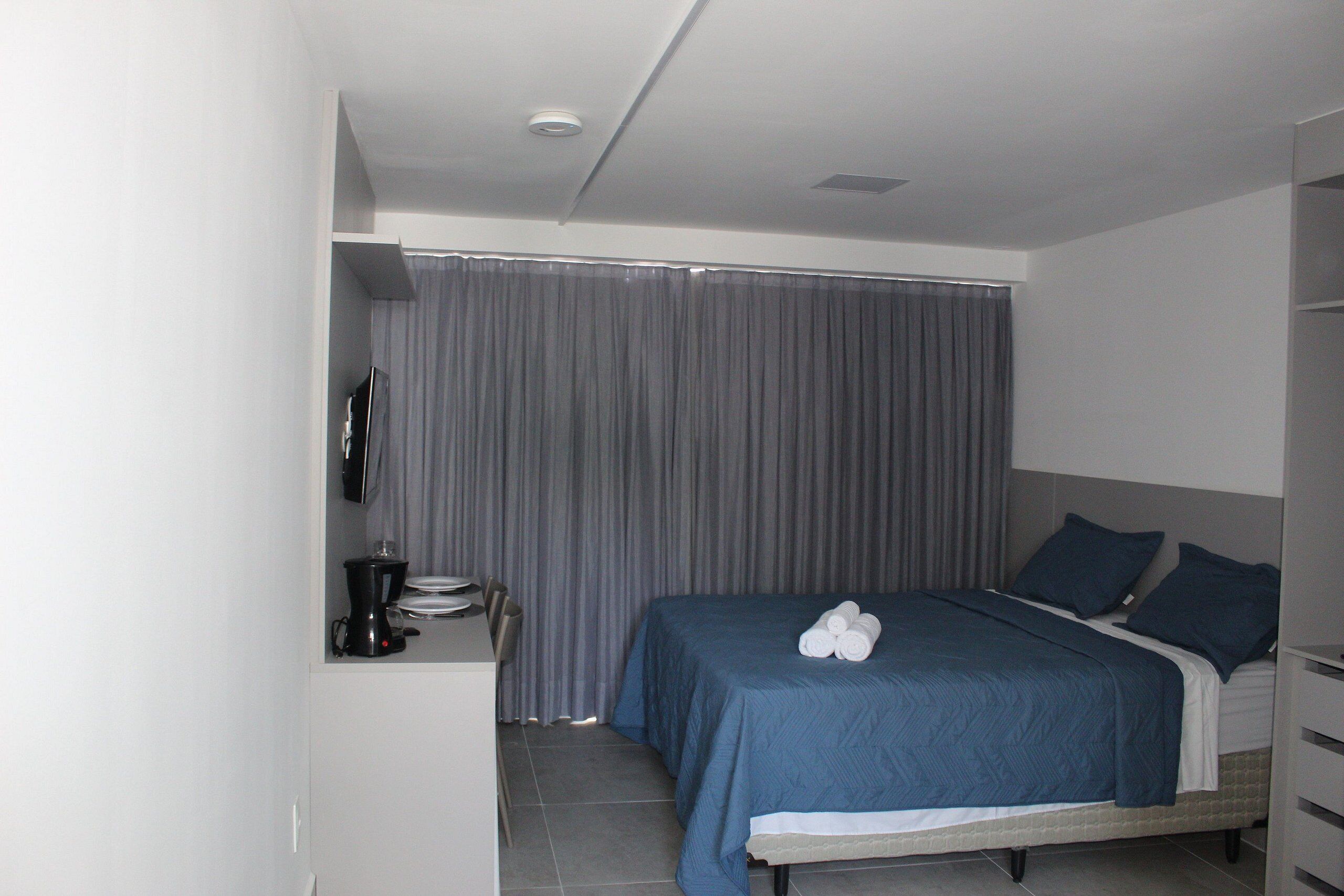 A modern hotel room with a neatly made bed, a small desk with a coffee maker, and a large window with curtains.