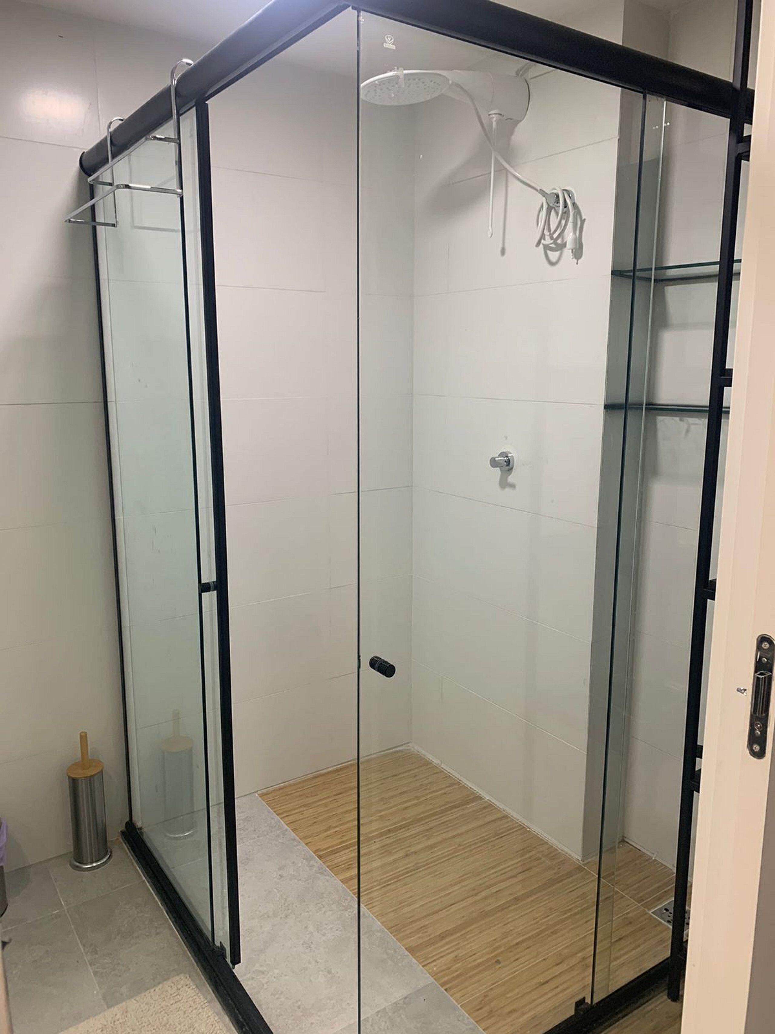 A glass-enclosed shower with a wooden floor, a visible showerhead, and a metal handle.